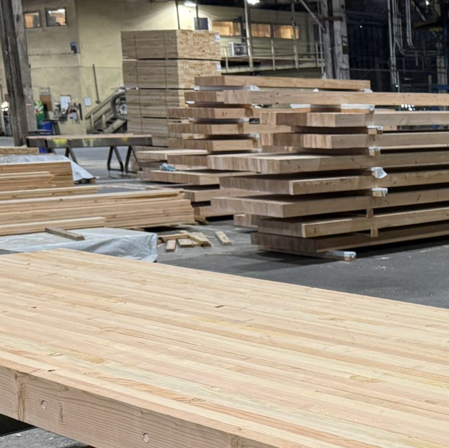 DLT panels in a manufacturing facility, showing the laminated softwood structure in the foreground and stacks of finished panels behind.